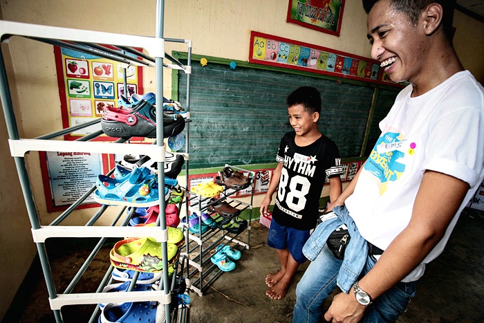 An employee volunteer from The SM Store Cauayan assists a kid in choosing his new pair of shoes. 